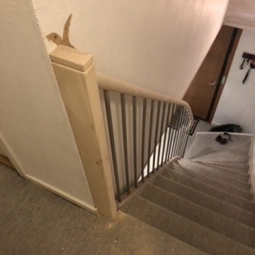 En trappe med gråt tæppe og et kombineret gelænder af lyst træ og stålstænger i et moderne interiør.