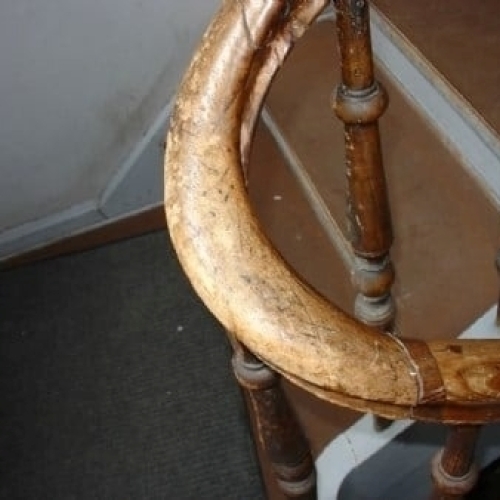 Et gammelt, slidt gelænder i træ med afskallet lak og tydelige brugsspor på en ældre trappe.