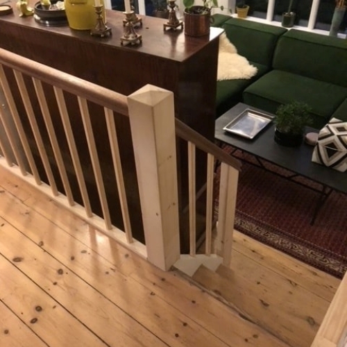 En trappe med nyt gelænder i lyst træ og mørk håndliste, der matcher det varme trægulv i stuen.