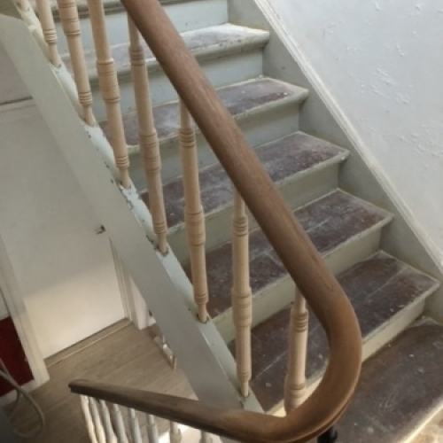 En enkel trappe med lyst trægelænder, der fører ned til en kælder med klinkegulv og hvidmalede vægge.