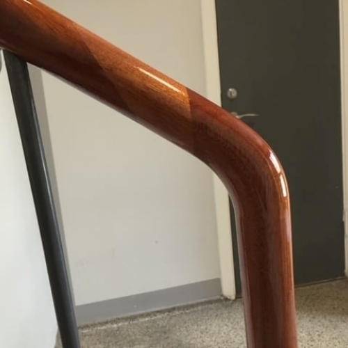 Et nypoleret, blankt gelænder i mørkt træ på en trappe med stålsøjler, set i nærbillede.