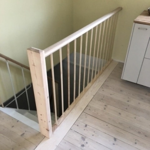 Et klassisk hvidmalet gelænder med profilering og sort håndliste, ved en trappe med sildebensmønstrede trin.