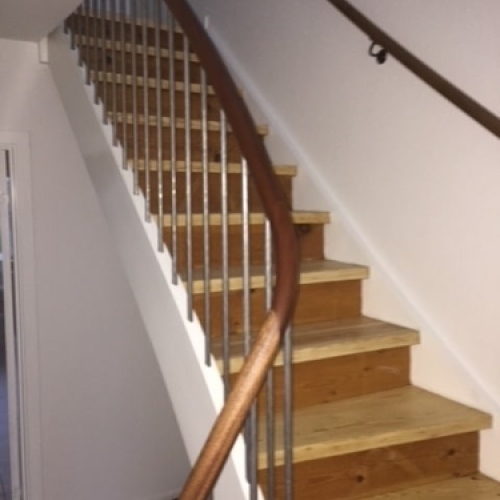 En moderne trappe med egetræstrin, stålsøjler og et slankt gelænder i mørkt træ for et minimalistisk udtryk.