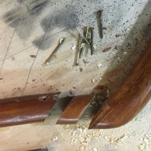 Et ødelagt gelænder i mørkt træ på et arbejdsbord med skruer og savsmuld, klar til reparation.