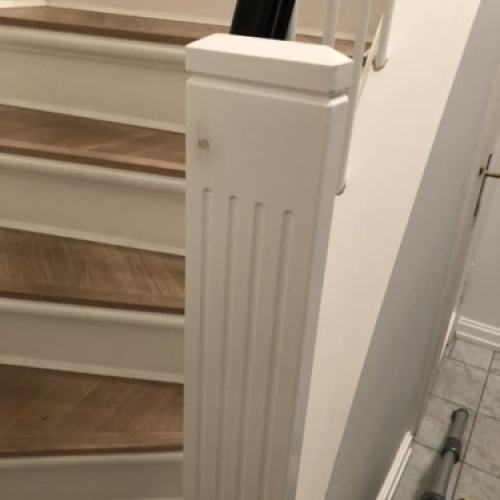 Et moderne gelænder i lyst træ og stålstænger langs en trappe med tæppebelægning, under montering.