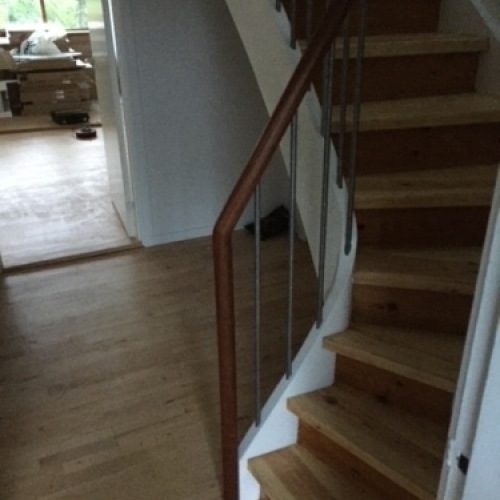 Udsigt ovenfra af en trappe med buet gelænder i lyst træ, der følger trappens form og passer til de lyse vægge.